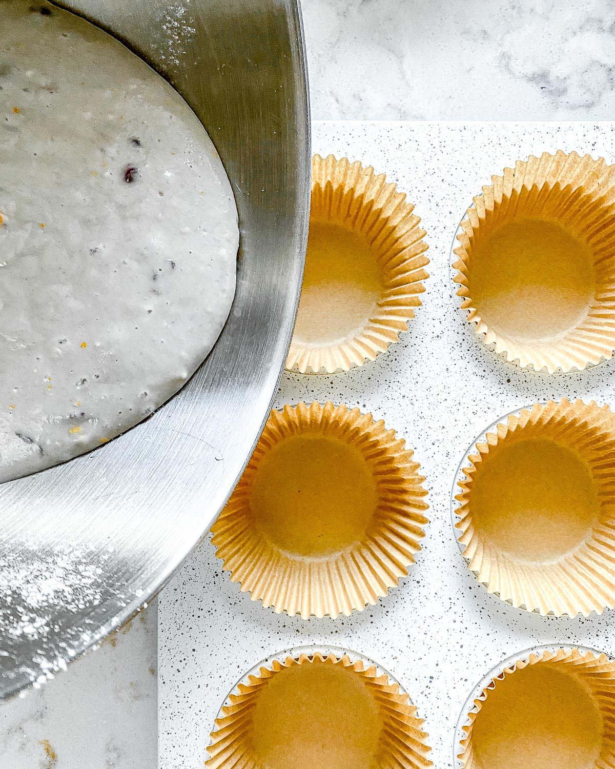 Process showing the pouring of blackberry orange cupcake batter into muffin tin.