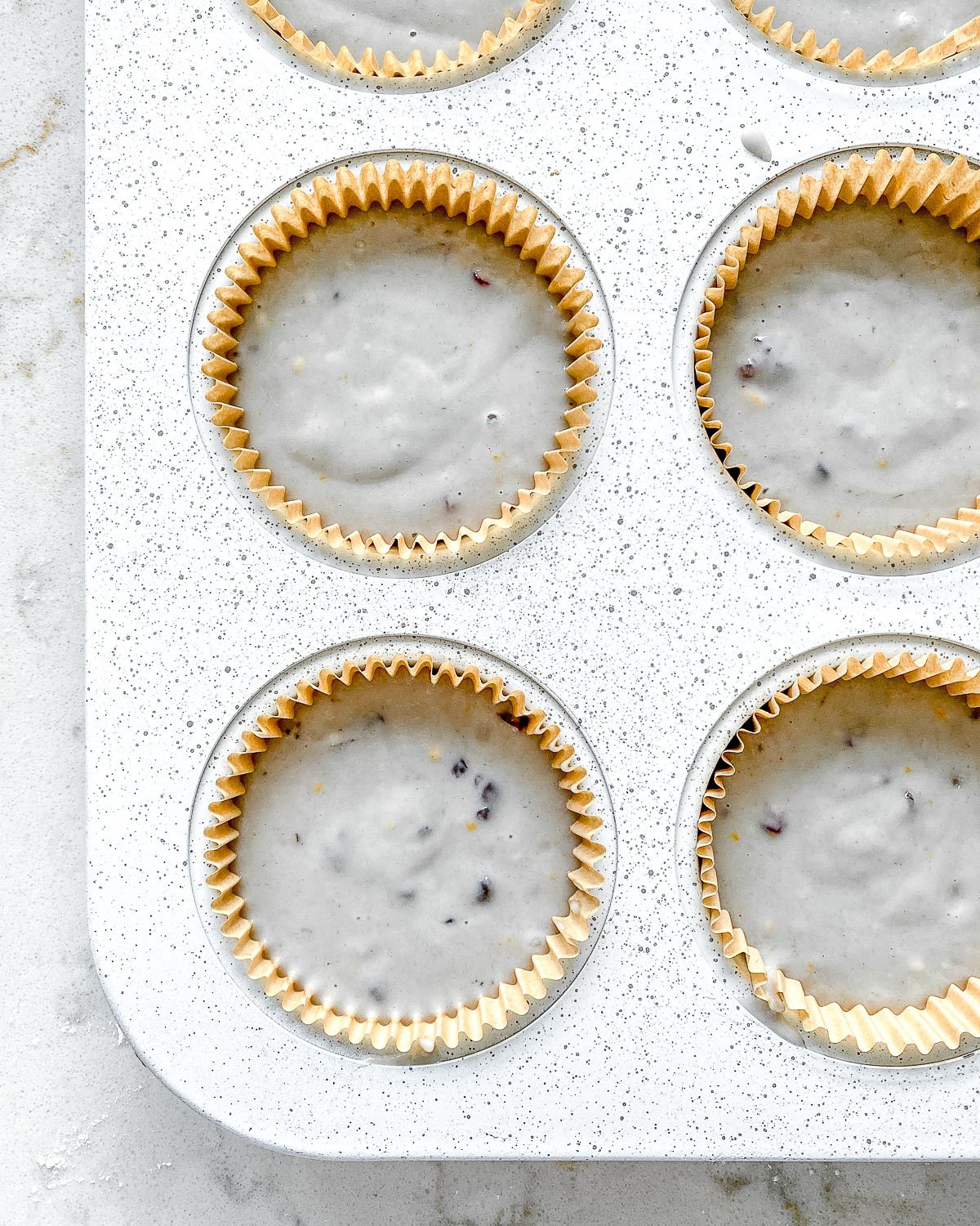 Process shot showing unbaked blackberry orange cupcakes in muffin tin prior to being baked.