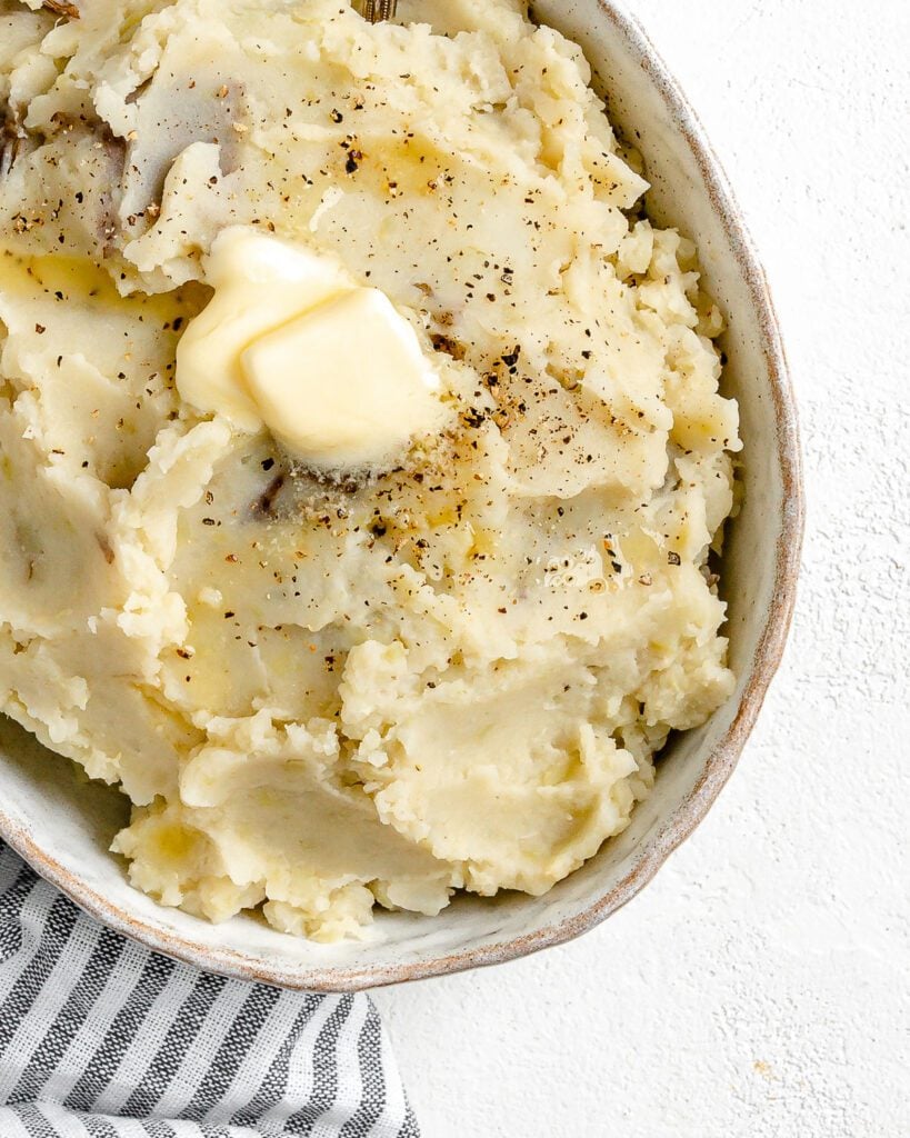 completed instant pot garlic mashed potatoes in a baking dish against a white background with a gray stripped towel in the background