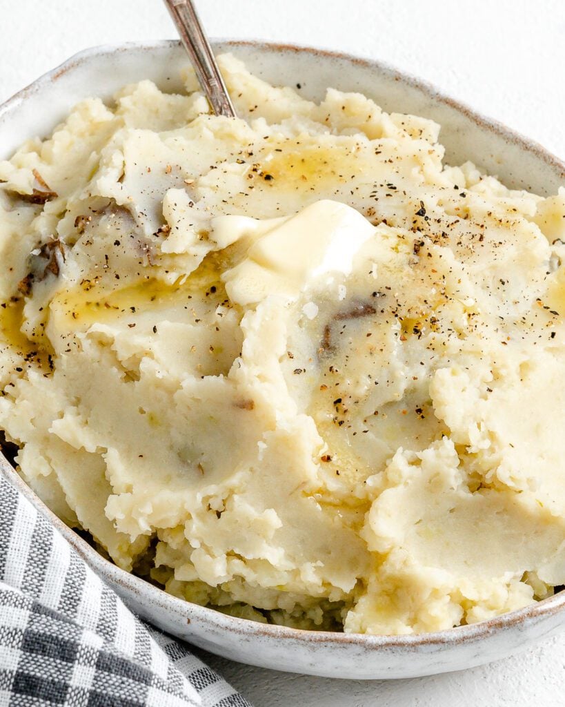 completed instant pot garlic mashed potatoes in a baking dish against a white background with a gray stripped towel in the background