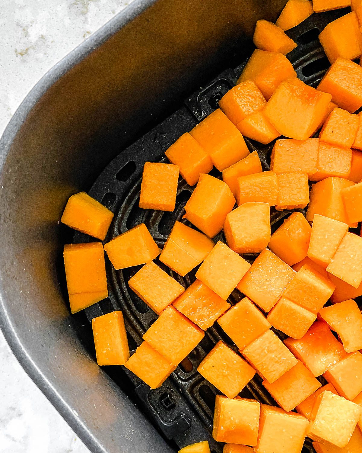 Process shot showing pre-cooked Simple Air Fryer Butternut Squash laid out in an air fryer basket.