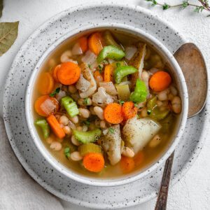 completed Instant Pot Navy Bean Soup in a white bowl on top of a plate against a white background
