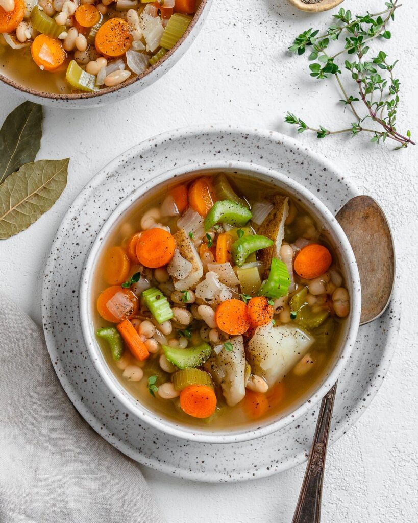 completed Instant Pot Navy Bean Soup in a white bowl on top of a plate against a white background