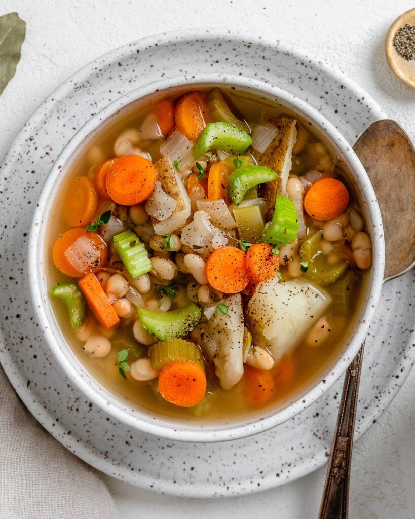 completed Instant Pot Navy Bean Soup in a white bowl on top of a plate against a white background