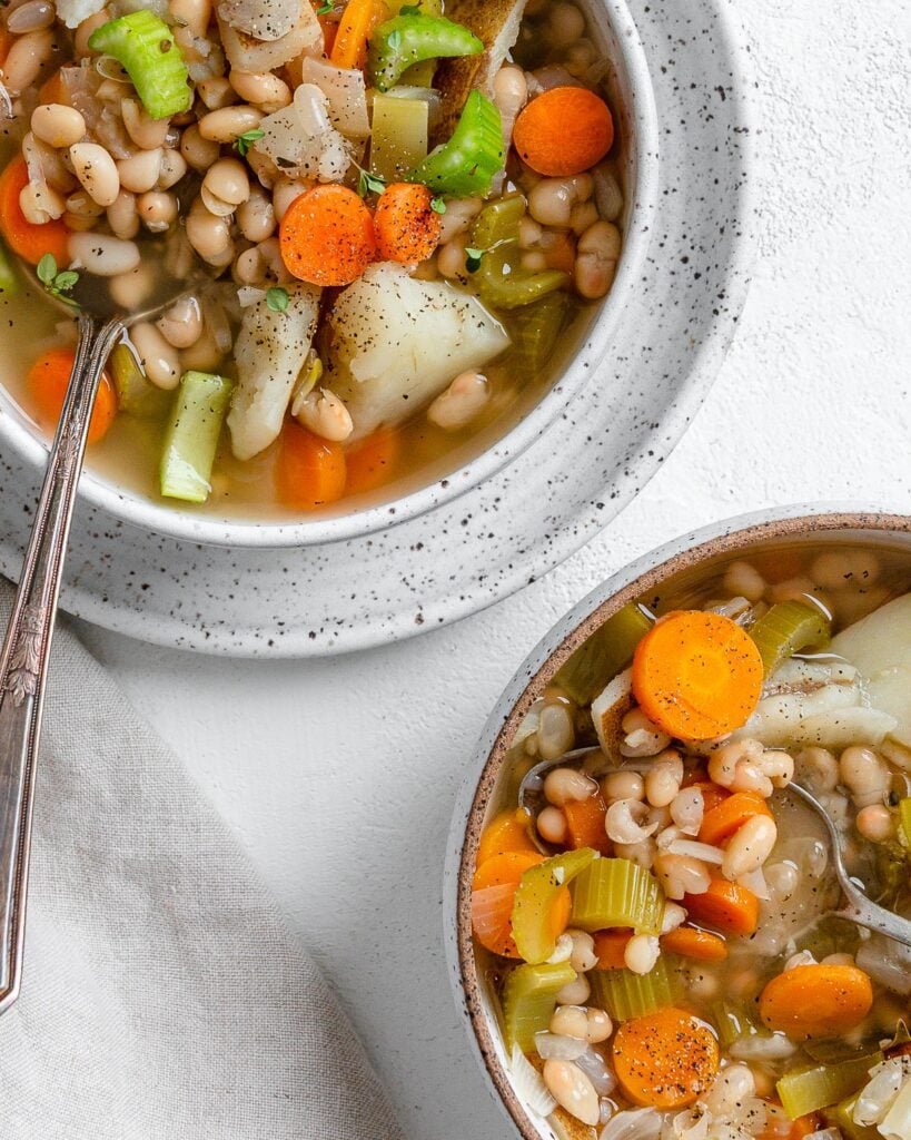 completed Instant Pot Navy Bean Soup in a white bowl on top of a plate alongside another bowl of soup against a white background