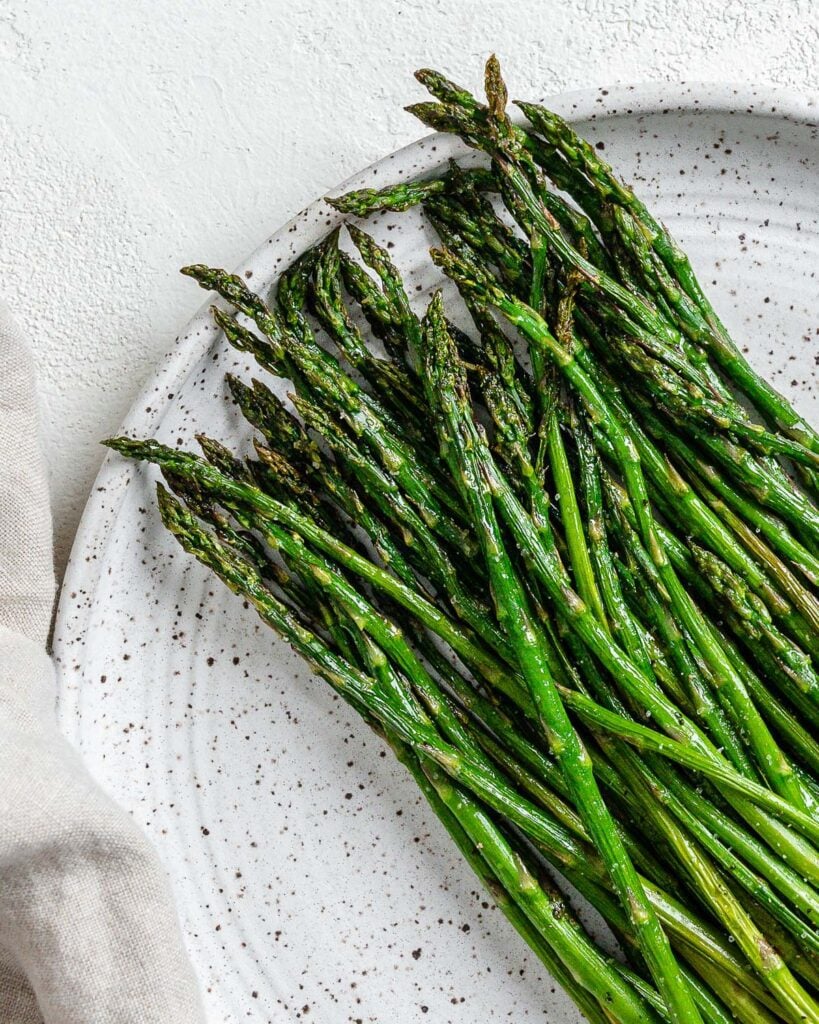 Completed air fryer asparagus on a white speckled plate.