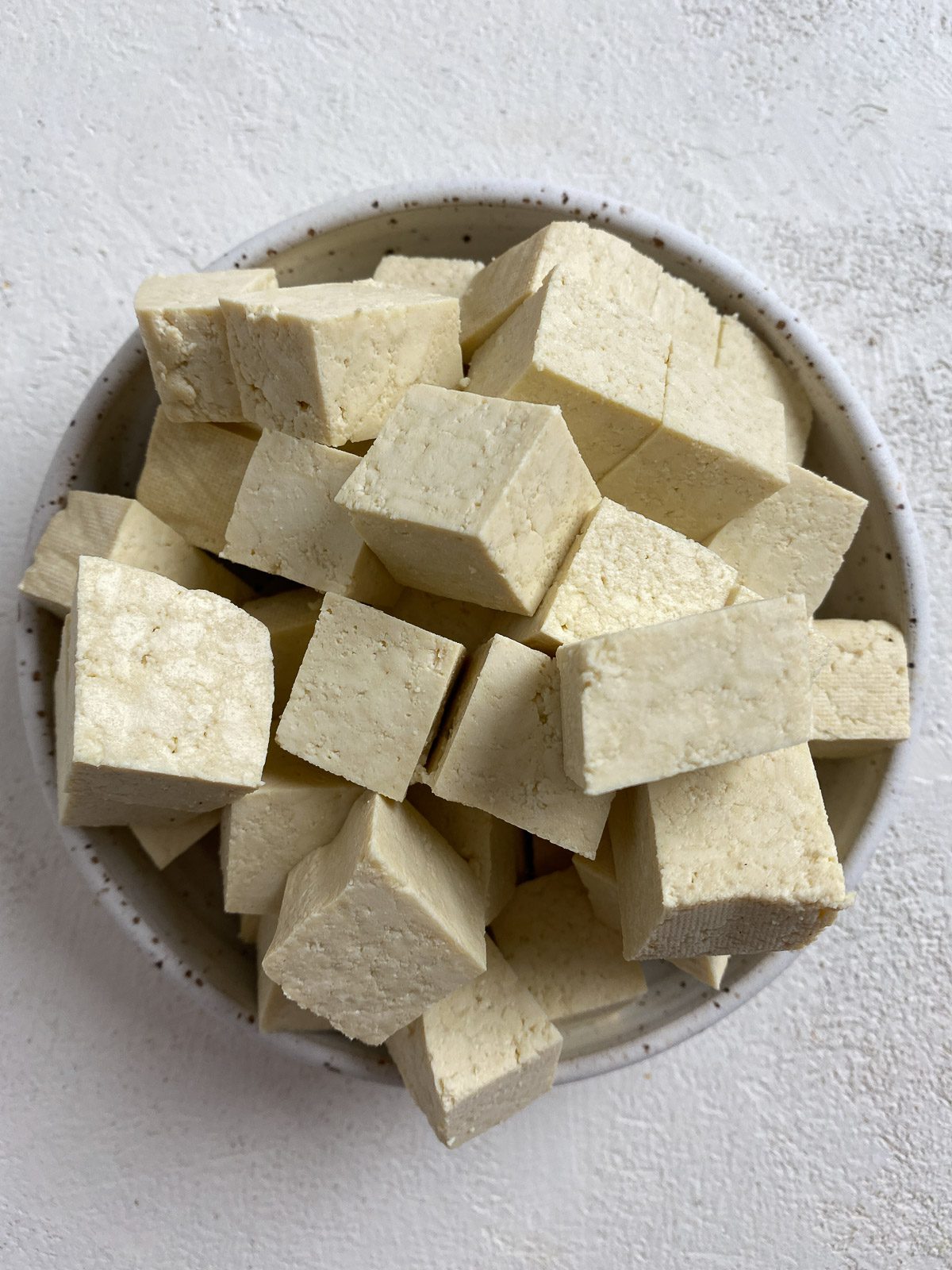 Cubed tofu in a white bowl against a white surface.