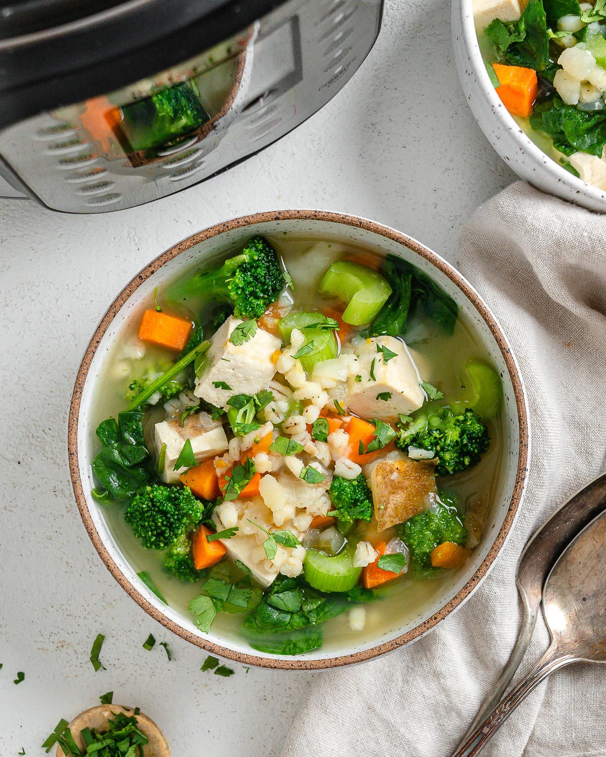 completed Instant Pot Vegetable Barley Soup in a white bowl against a white background with a pressure cooker in the background