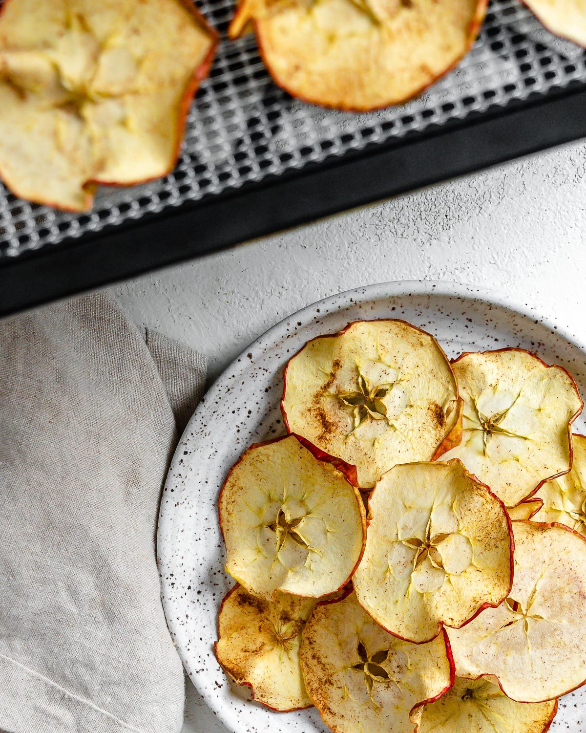 completed Dehydrator Apple Chips on a white plate with chips in the background