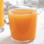 completed Apple OJ Carrot Juice in a glass against a white surface and light background