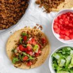 completed walnut chorizo tacos with chorizo and veggies in the background against a white surface