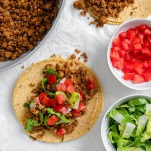 completed walnut chorizo tacos with chorizo and veggies in the background against a white surface
