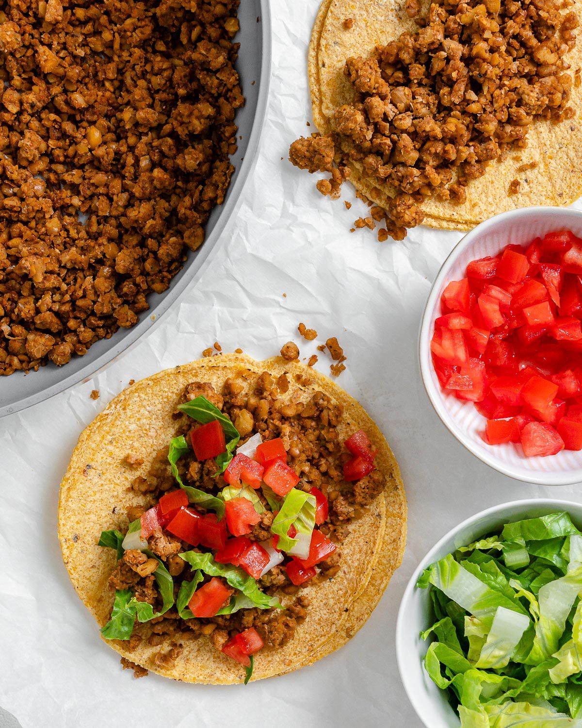 completed walnut chorizo tacos with chorizo and veggies in the background against a white surface