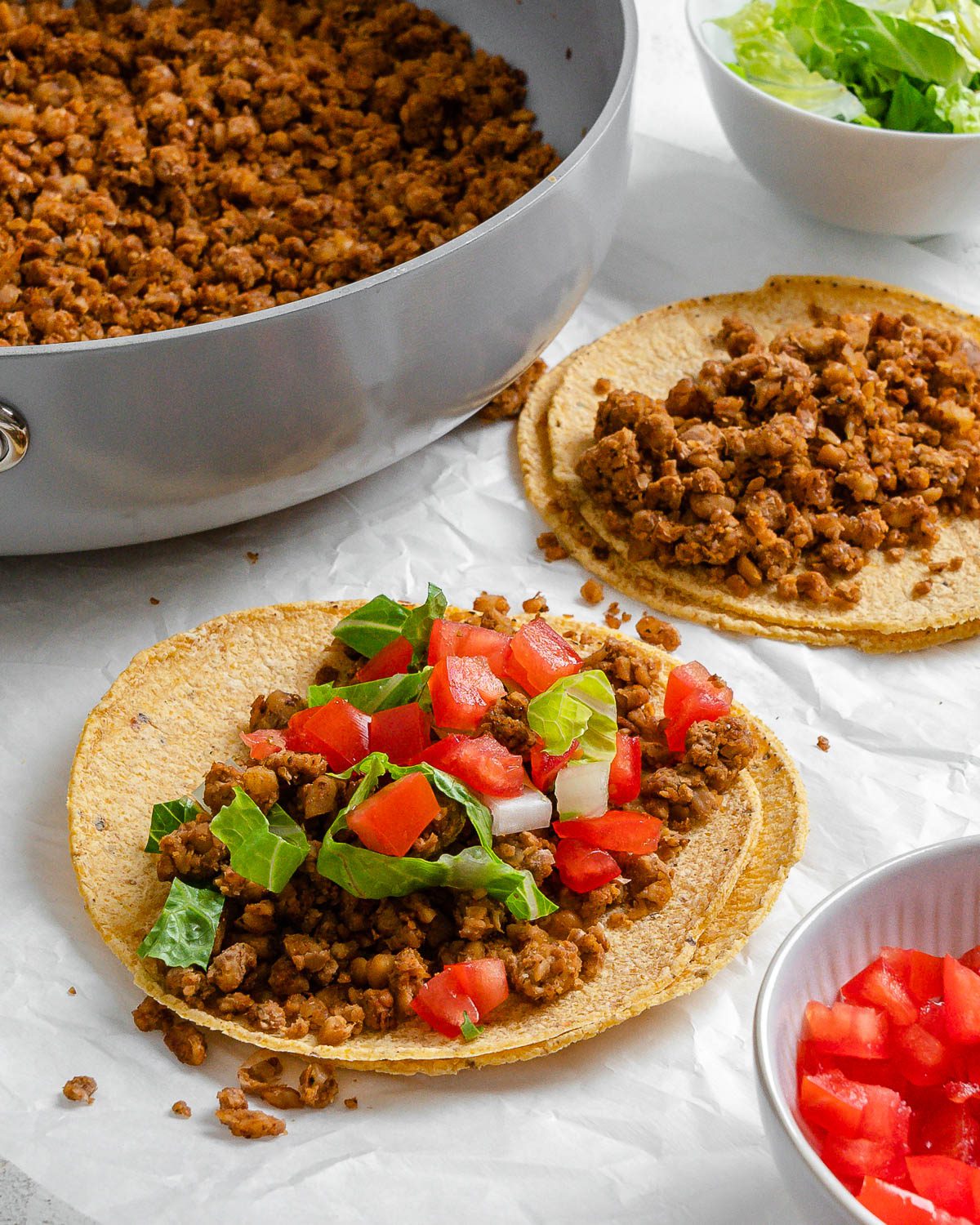 completed walnut chorizo tacos with chorizo and veggies in the background against a white surface