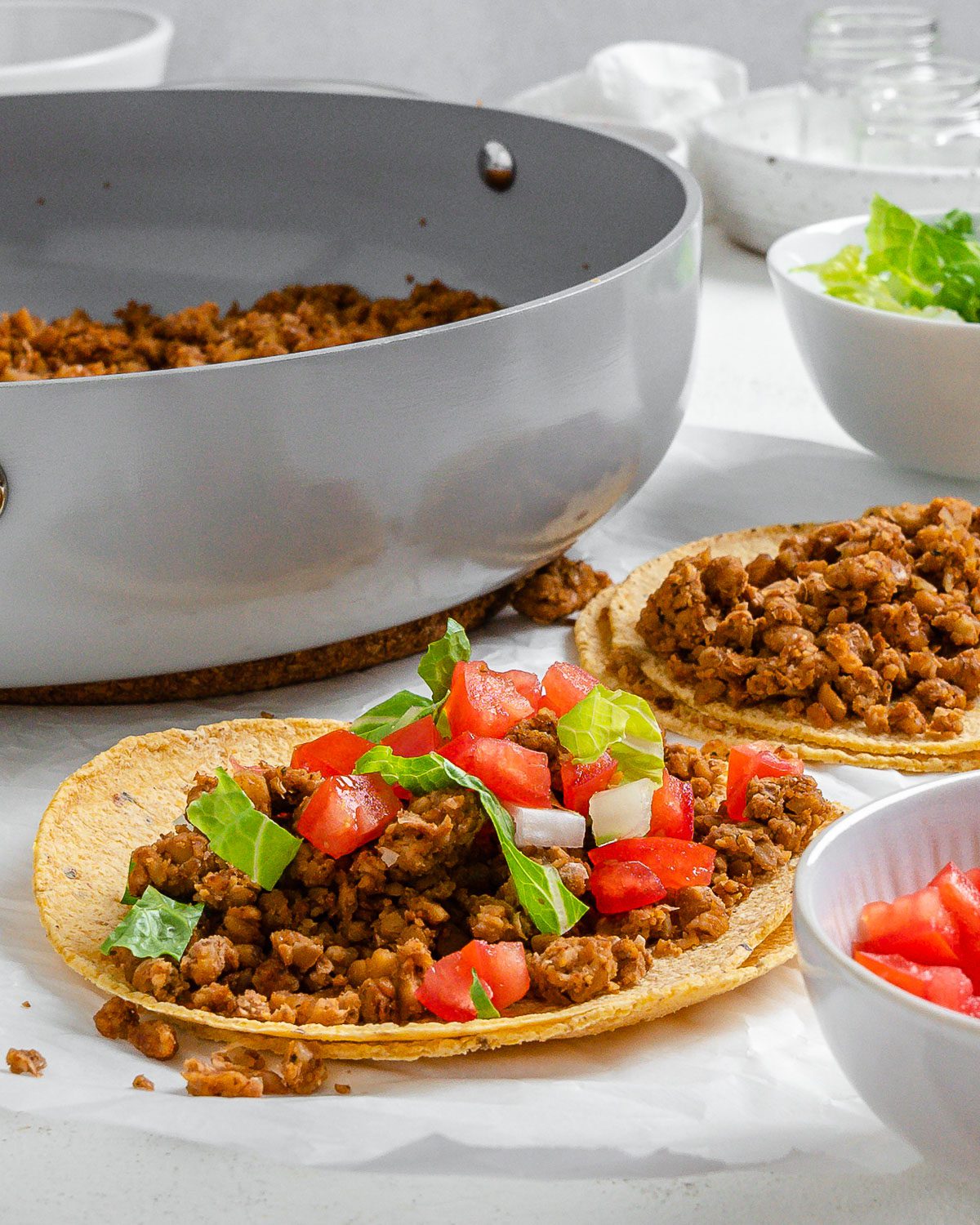 completed walnut chorizo tacos with chorizo and veggies in the background against a white surface
