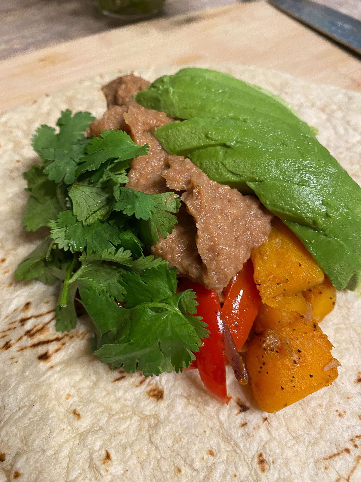 process of adding avocado and cilantro to burrito filling on tortilla