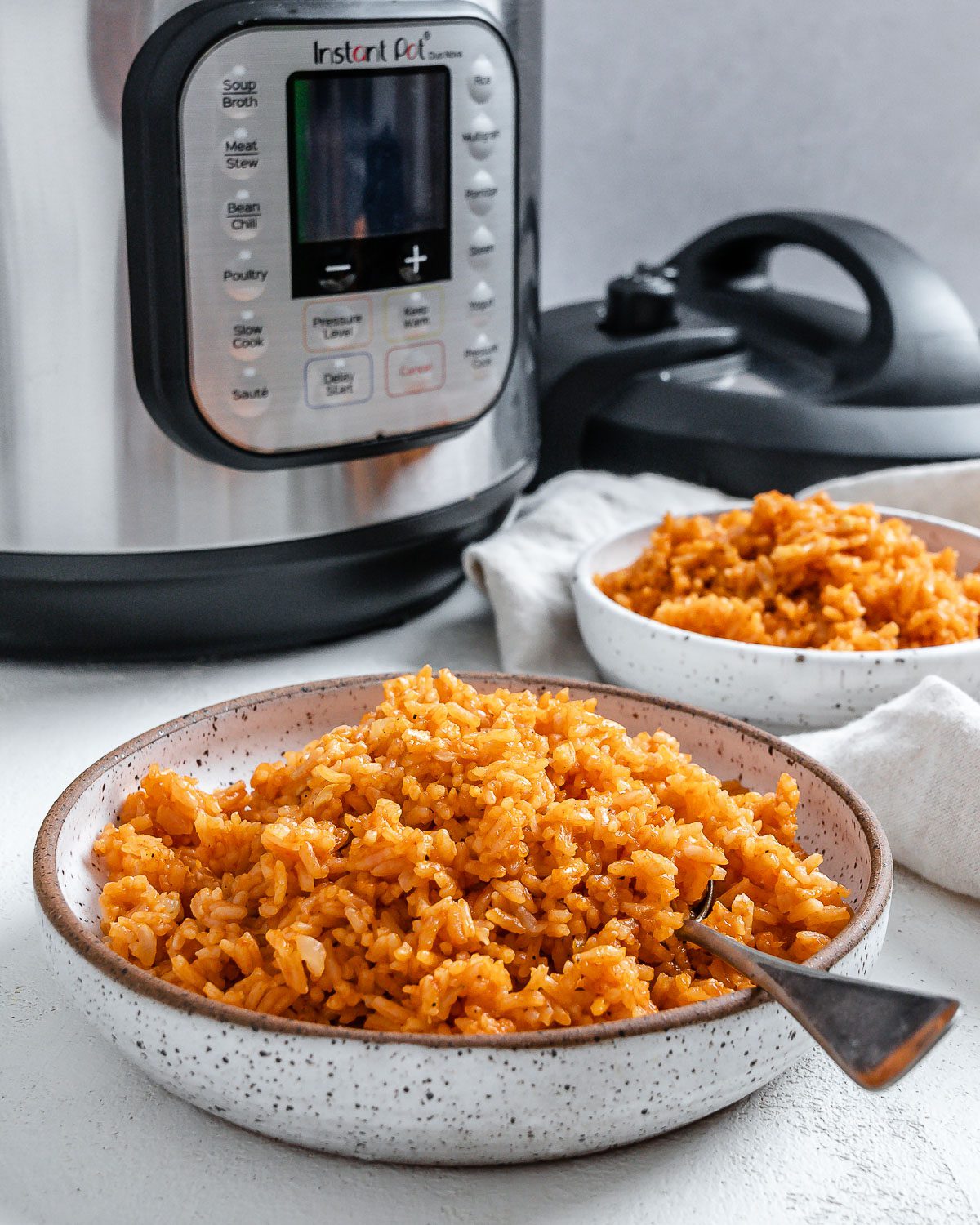 completed mexican rice in two white bowls against a white background with the instant pot in the back