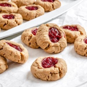 completed Vegan Peanut Butter and Jelly Thumbprint Cookies scattered on cookie sheet and white surface