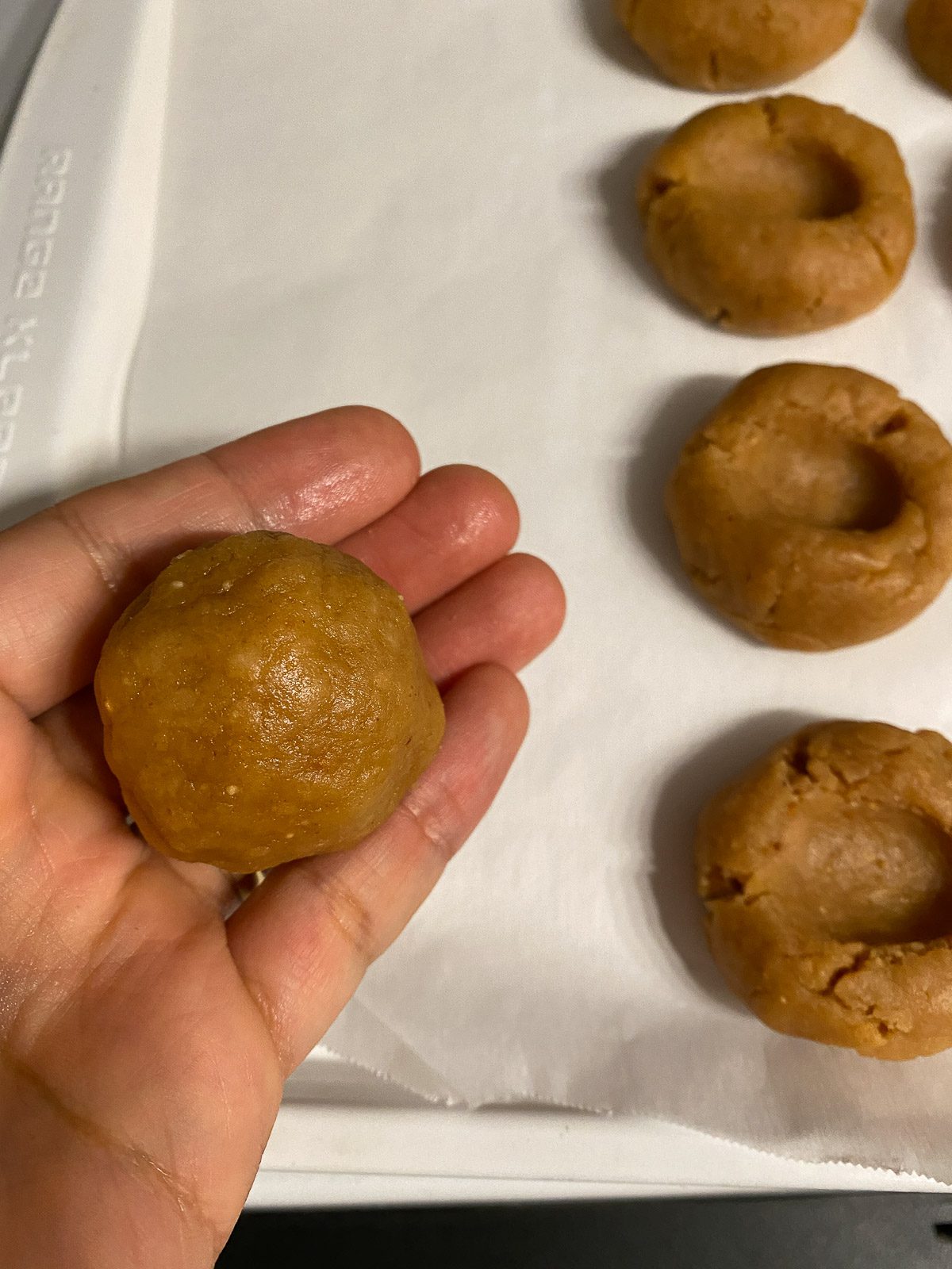 process of showing tablespoon of dough held in hand with thumbprint imprinted dough balls in the background