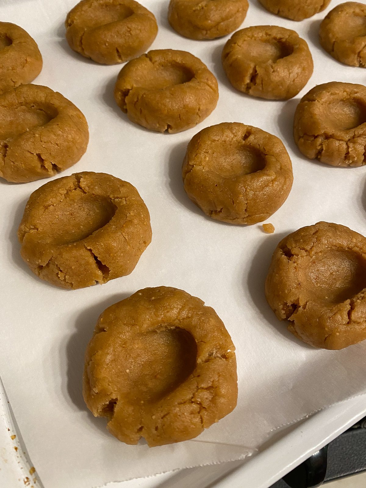 several thumbprint indented cookie dough pieces on a baking sheet