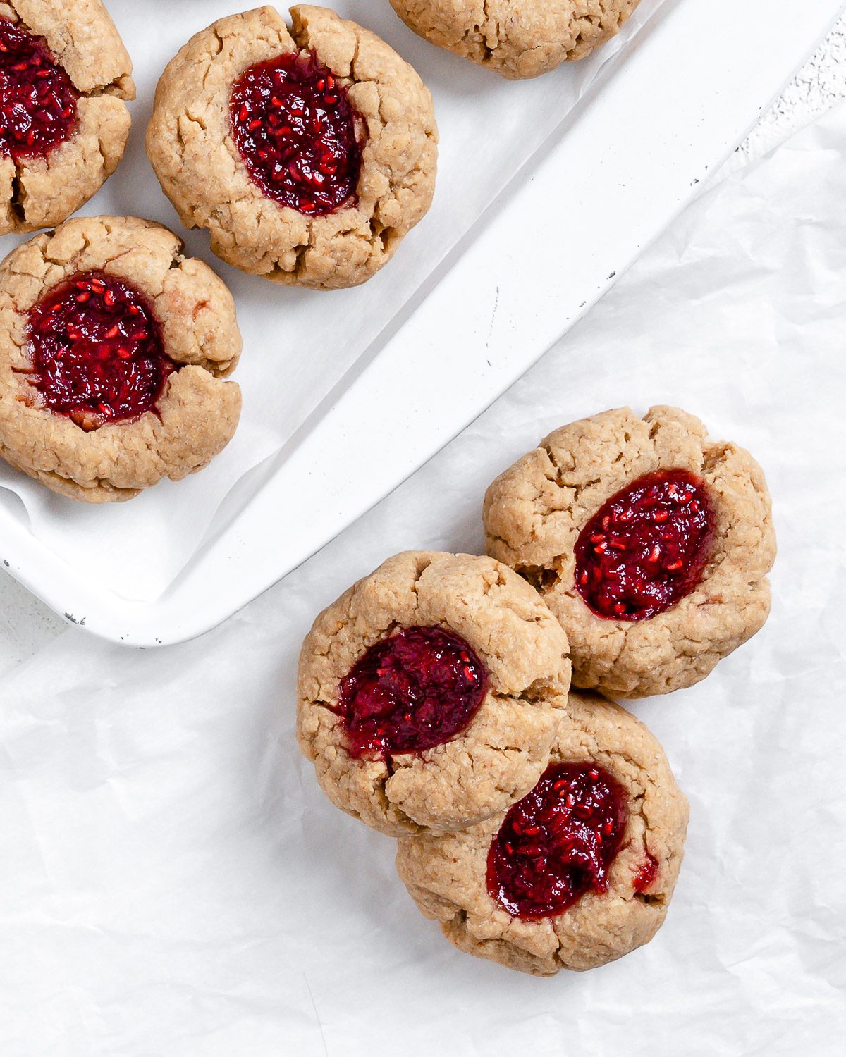 completed Vegan Peanut Butter and Jelly Thumbprint Cookies scattered on cookie sheet and white surface