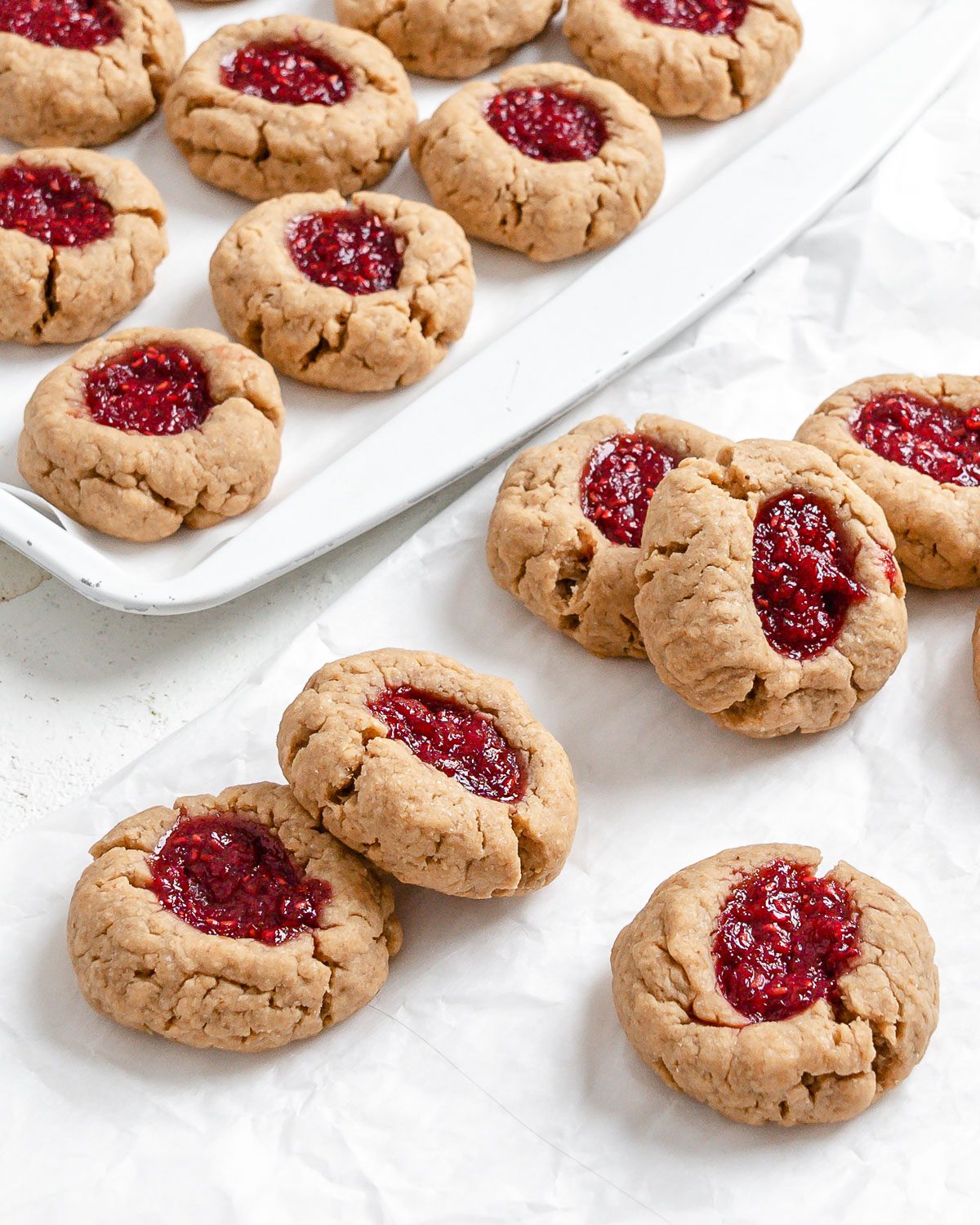 completed Vegan Peanut Butter and Jelly Thumbprint Cookies scattered on cookie sheet and white surface