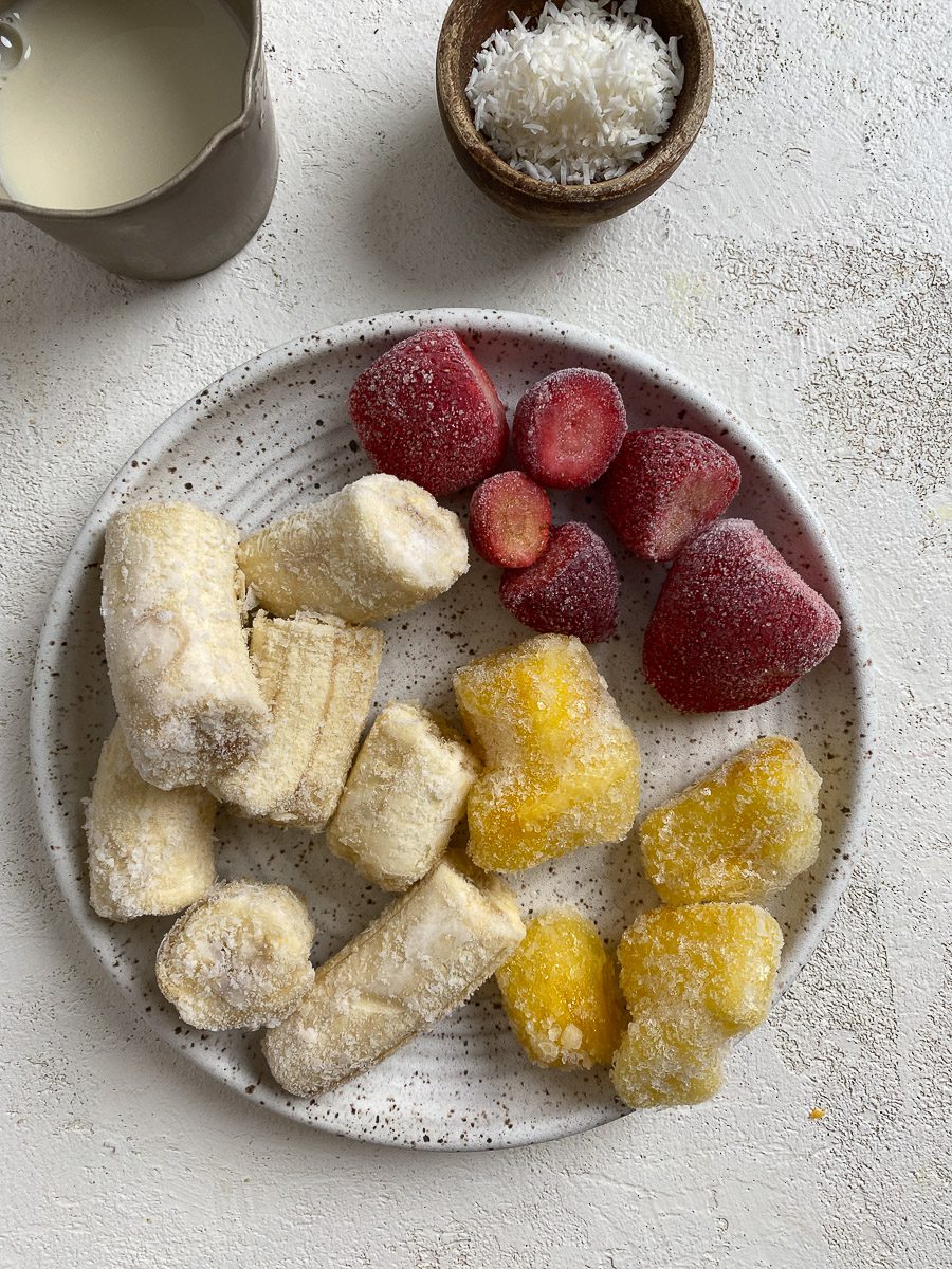 cut frozen bananas, strawberries, and pineapple on a white plate against a light background