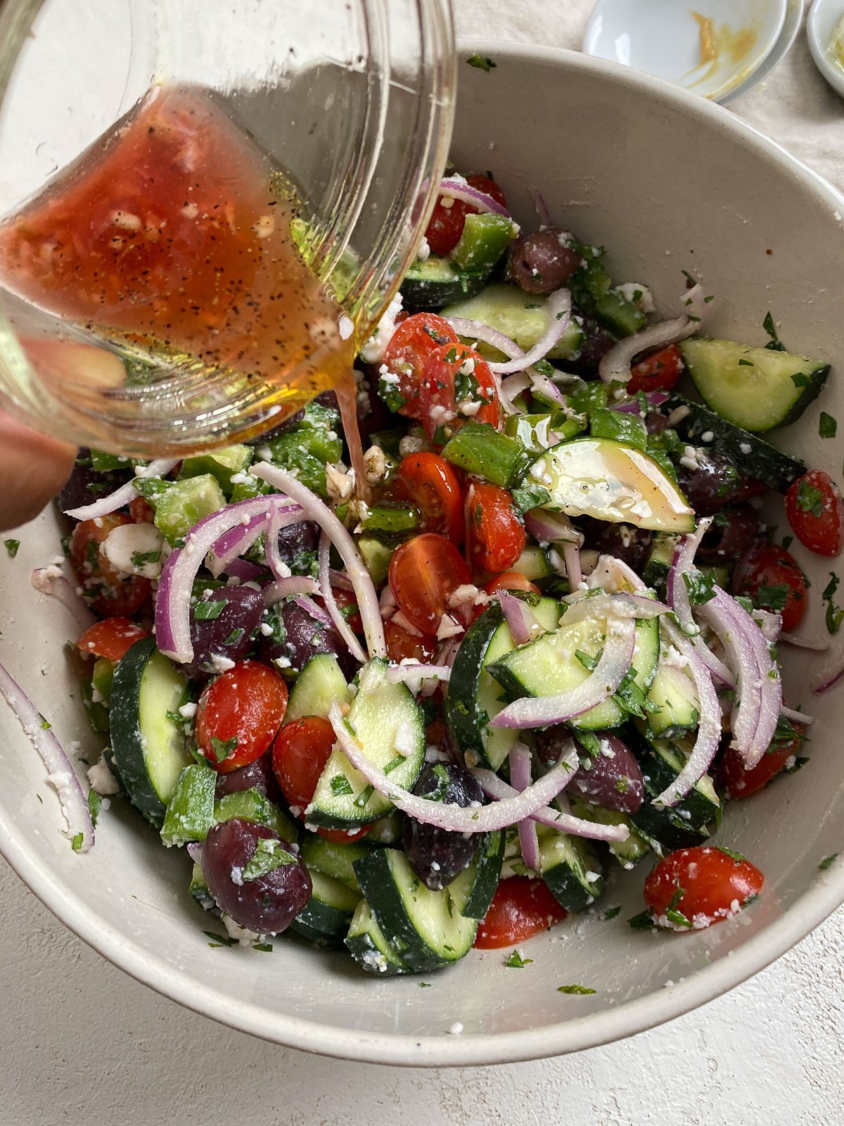 process shot showing the pouring of dressing onto bowl of vegan greek salad