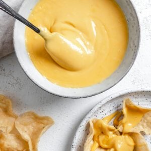 completed Vegan Nacho Cheese in a white bowl with chips in the background