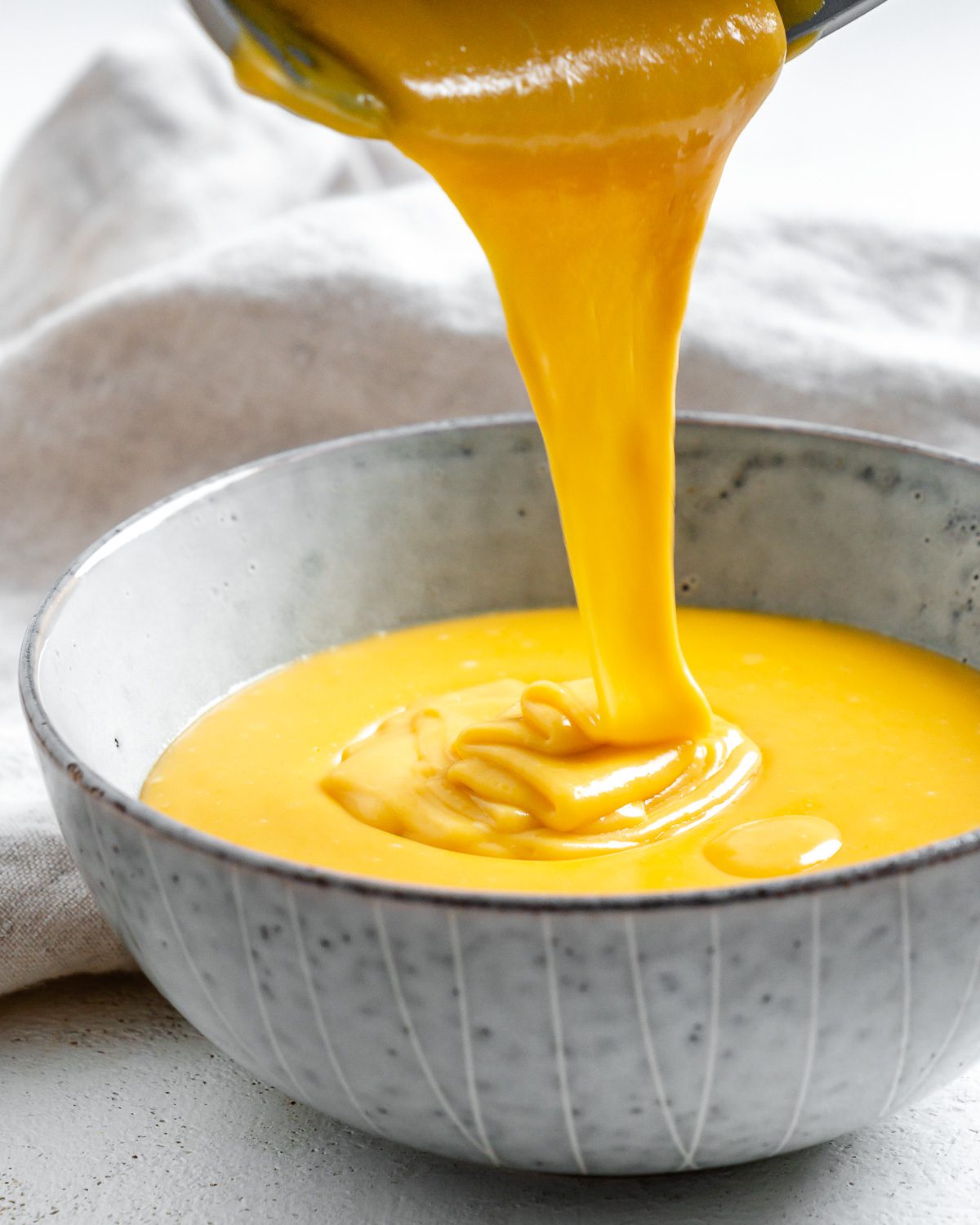 completed Vegan Nacho Cheese being poured into a white bowl