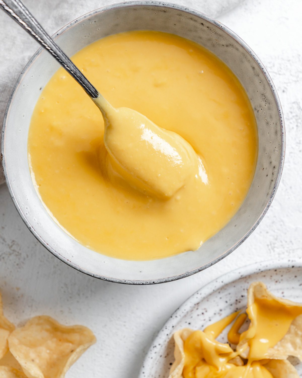 completed Vegan Nacho Cheese in a white bowl with chips in the background