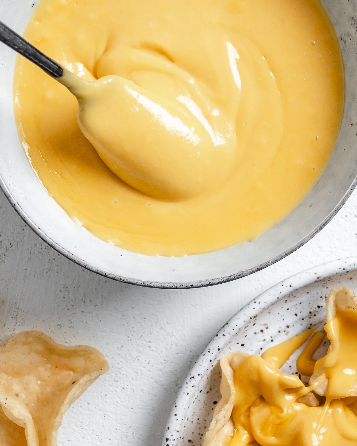 completed Vegan Nacho Cheese in a white bowl with chips in the background