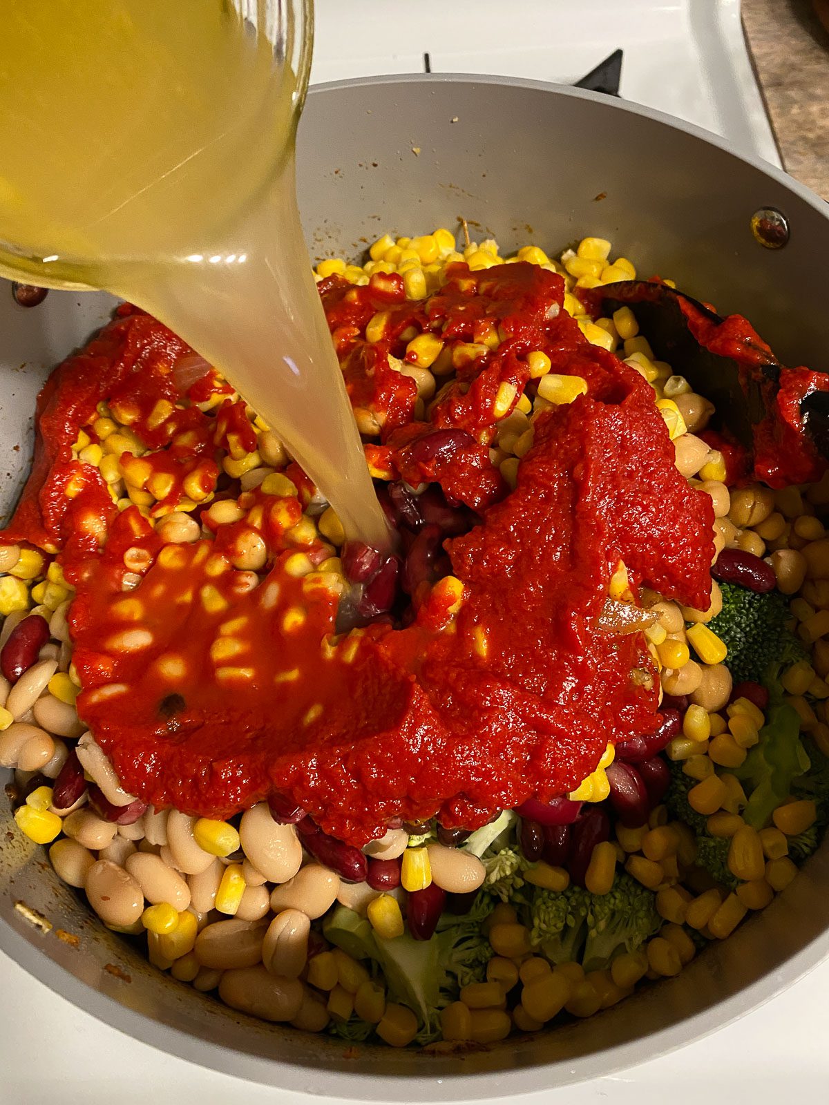 process of adding veggie broth into mixed pan of veggies