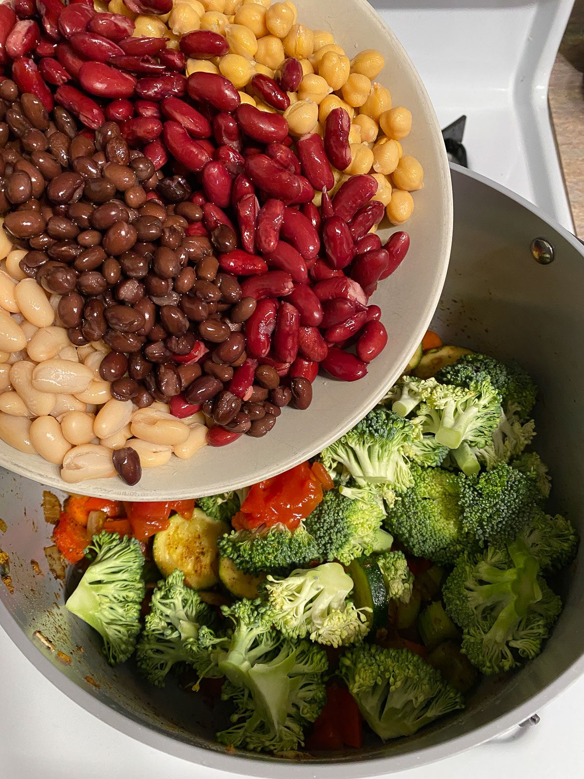 process of adding mixed beans to mixed pan of veggies