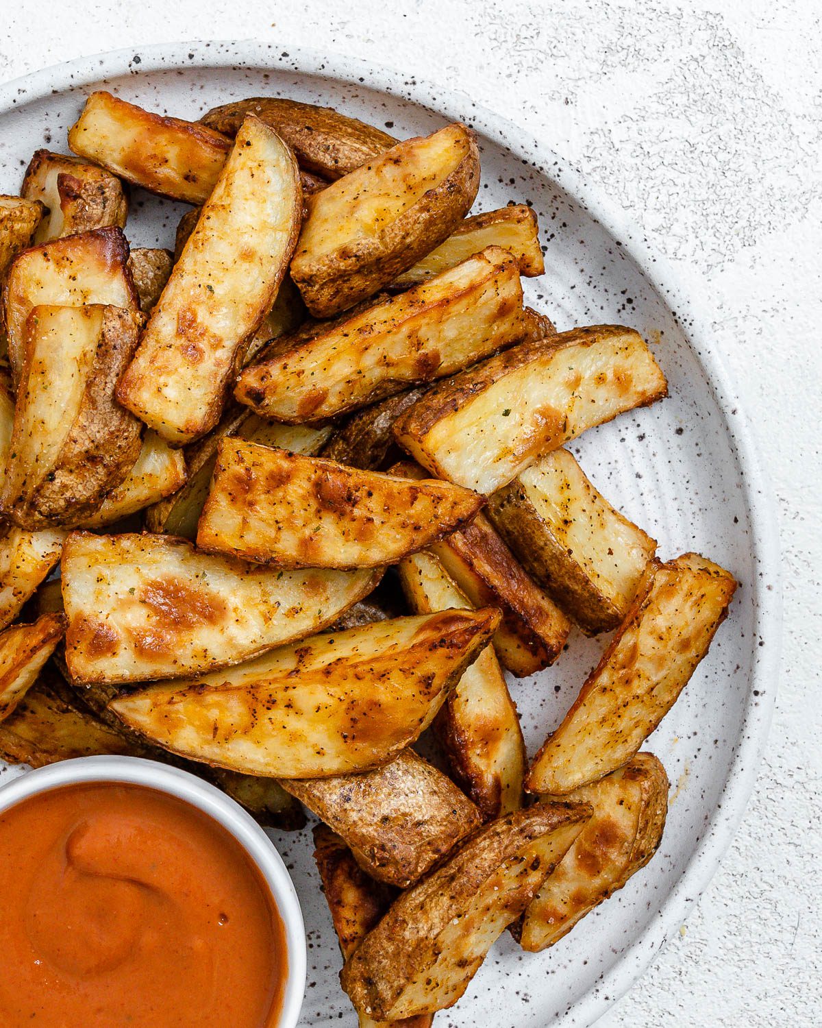 completed Air Fryer Potato Wedges plated on a white plate alongside a sauce