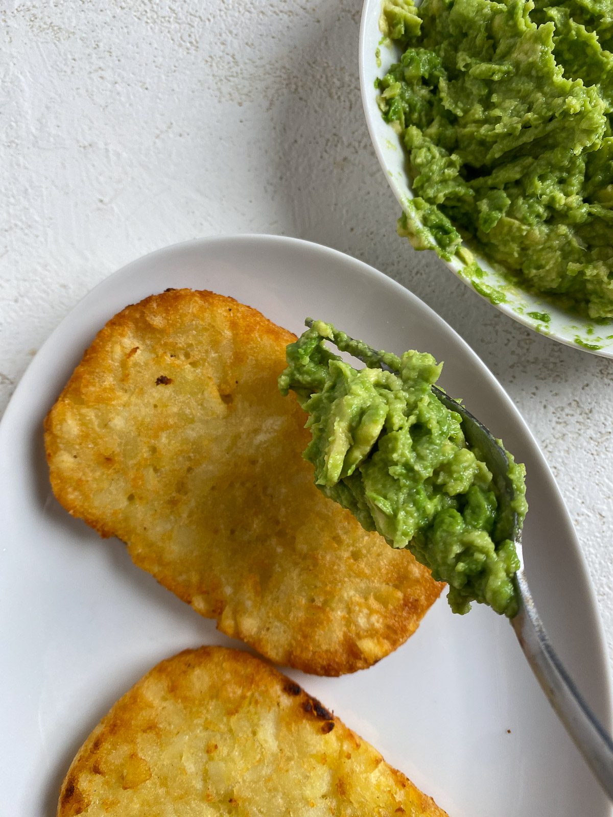 process of spreading smashed avocado on a hashbrown