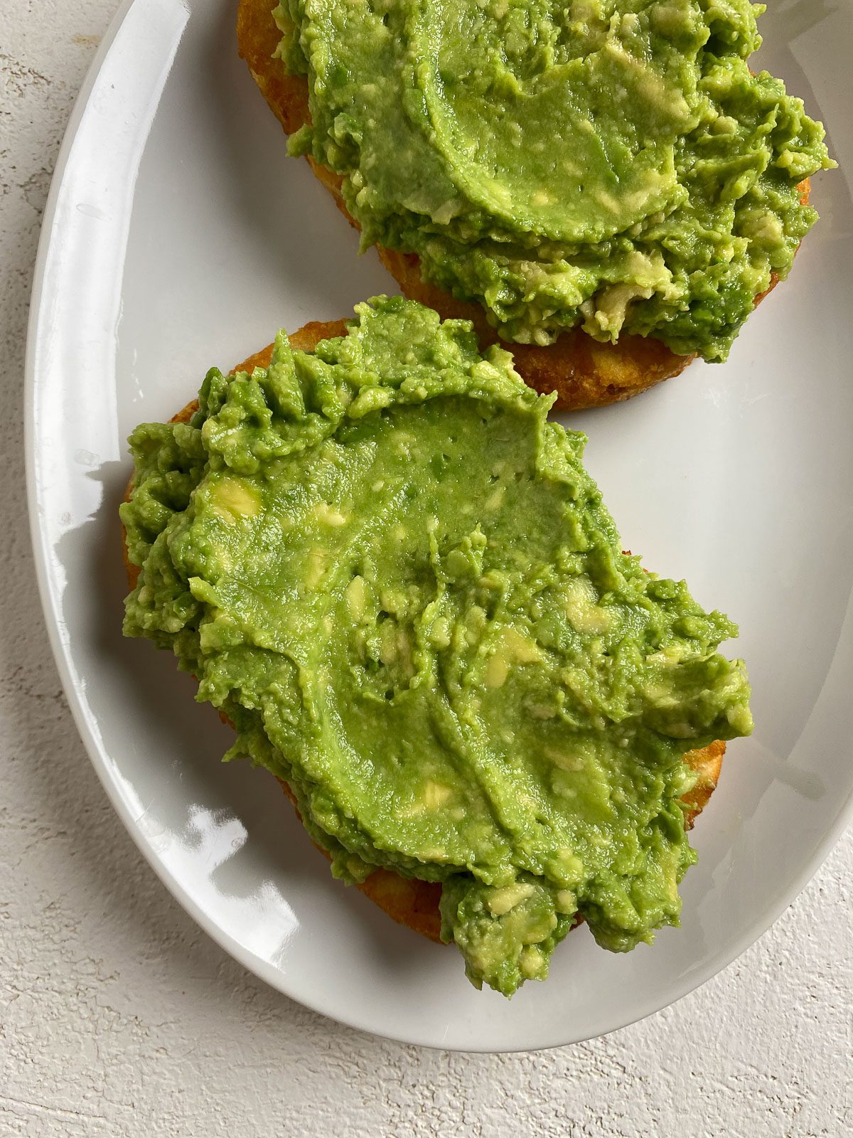 post applying avocado onto two slices of hashbrowns on a white plate