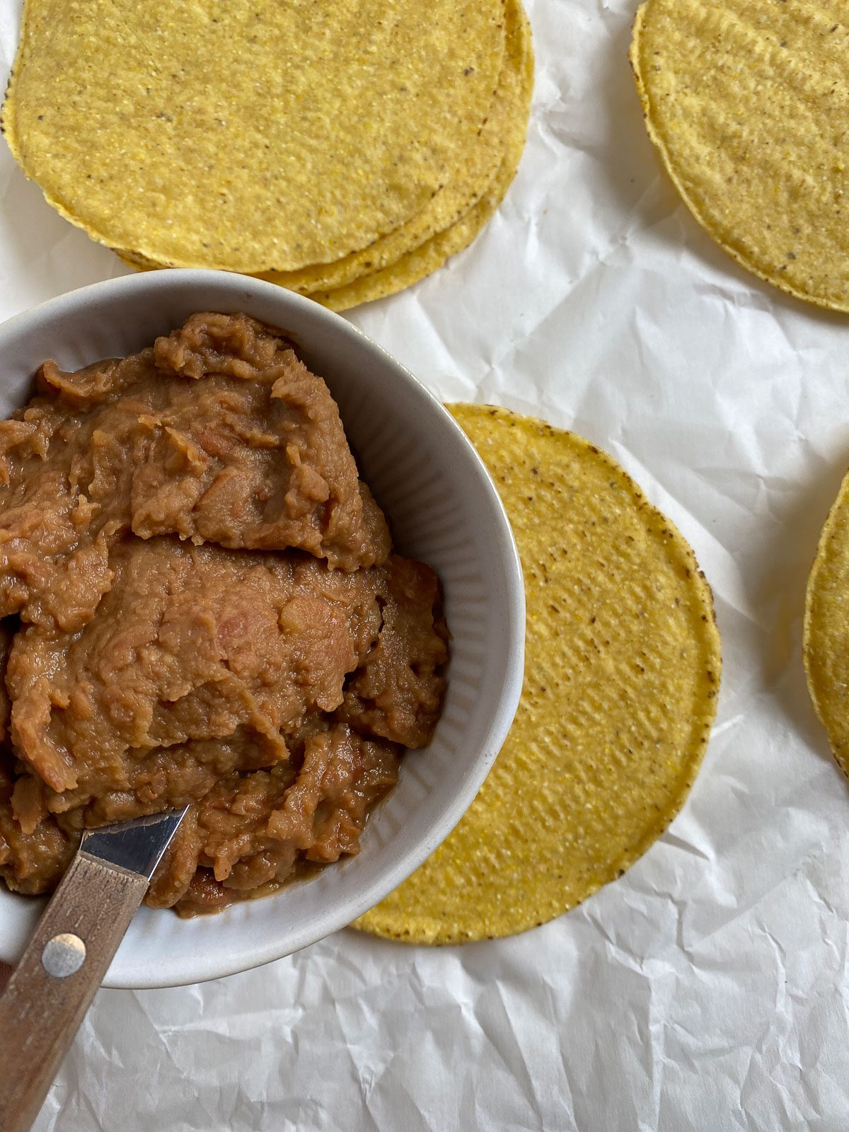 process shot of refried beans being spread onto a tostada shell
