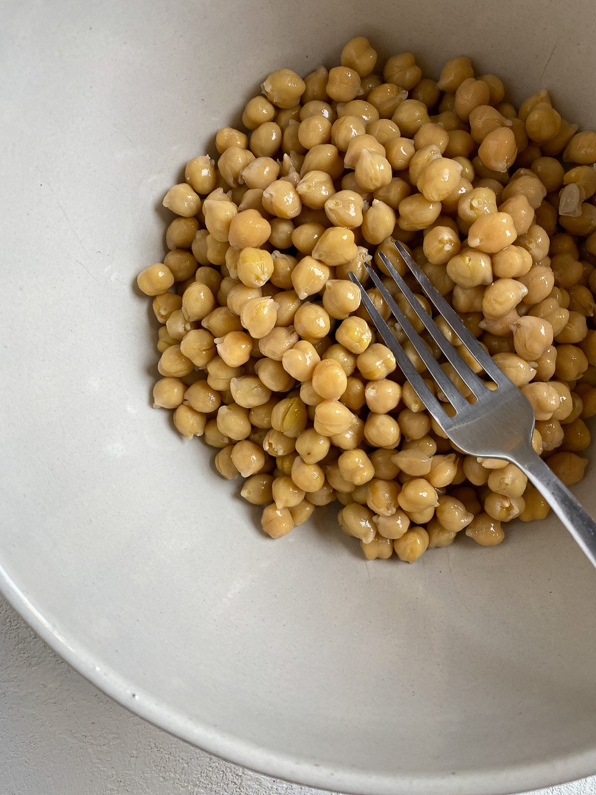 process shot of mashing chickpeas in a white bowl