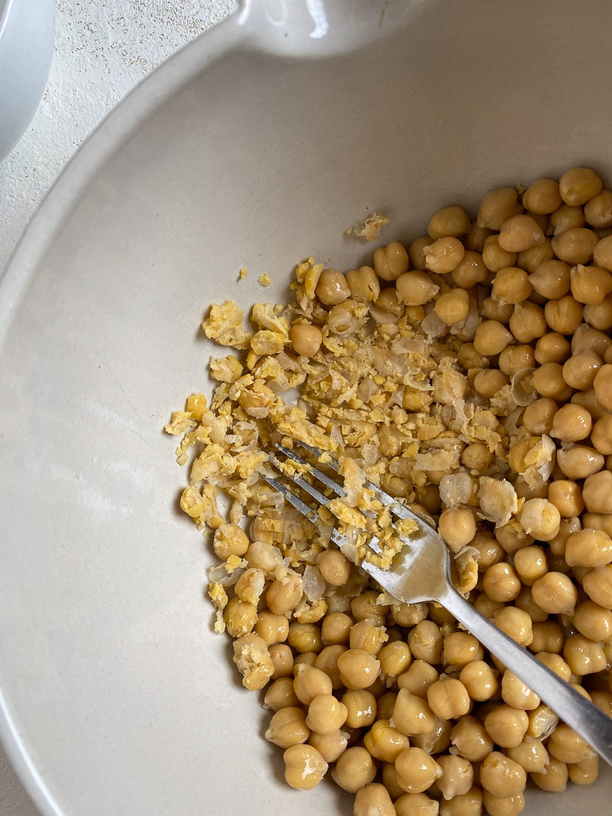 process shot of mashing chickpeas in a white bowl