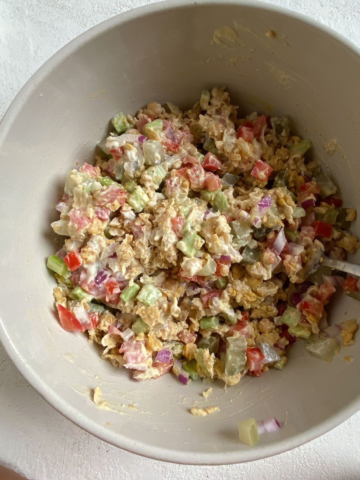 process of mixing additional ingredients for a vegan chickpea salad sandwich in a white bowl