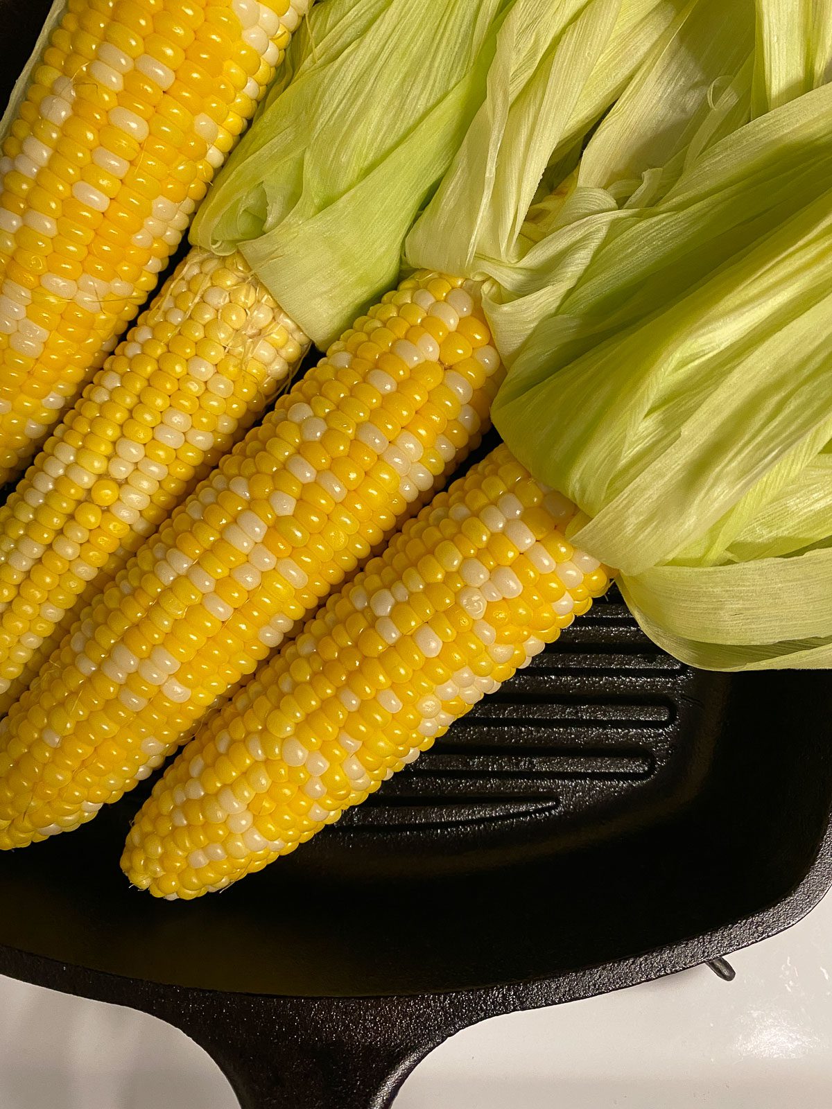 Four cobs of corn on a black skillet.