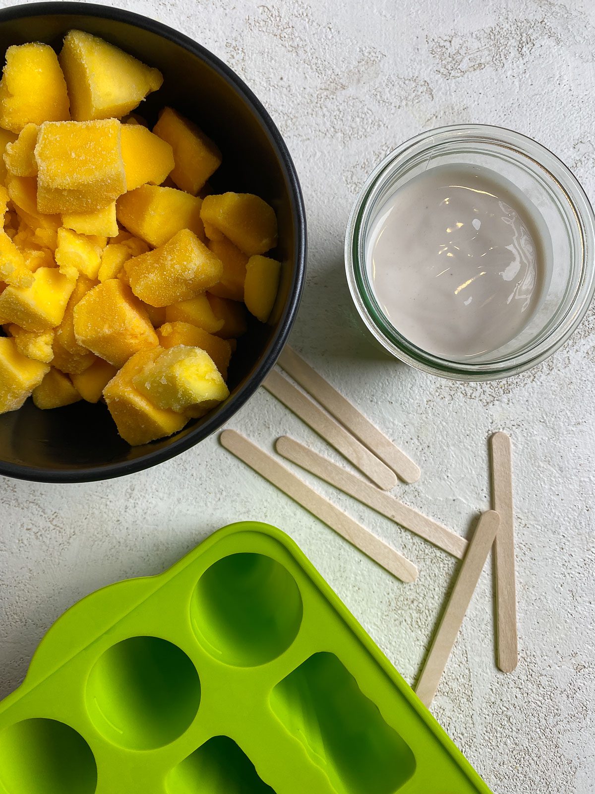 ingredients for Vegan Mango Popsicles alongside popsicle molds against a white surface