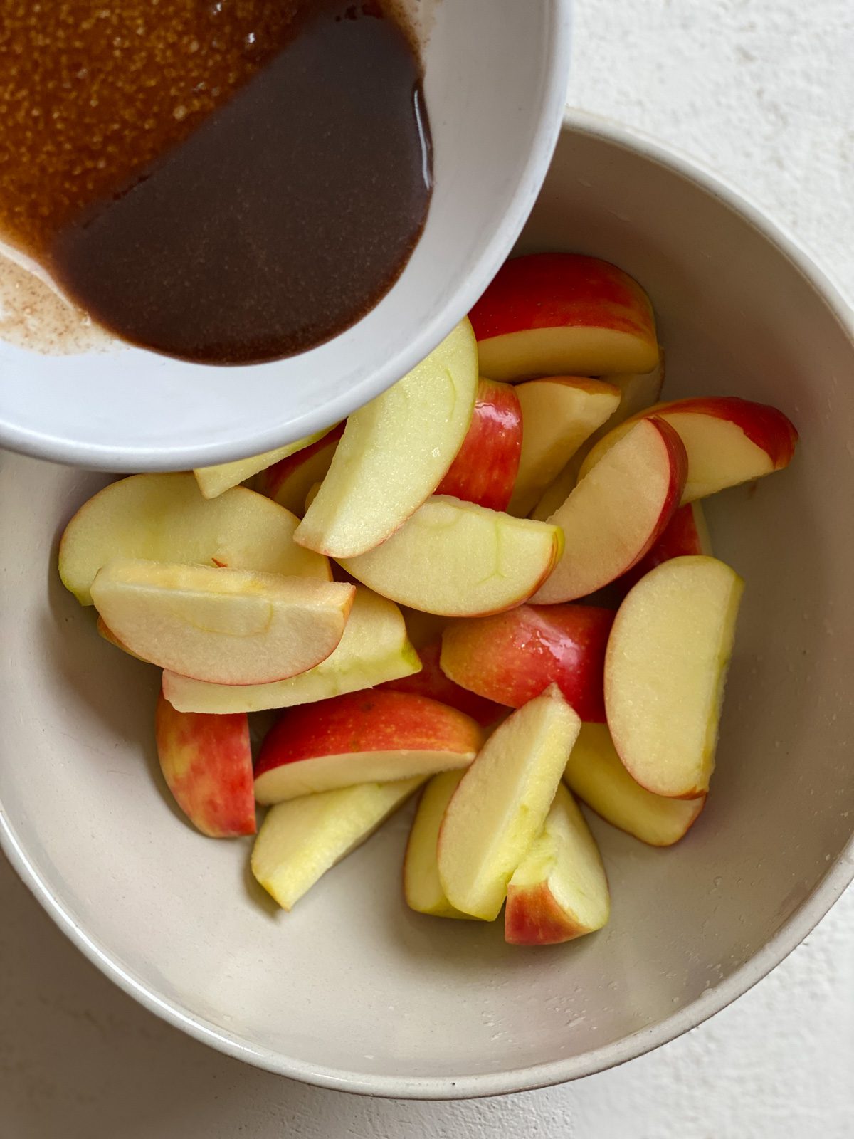 process shot of pouring air fryer apple topping on top of sliced apples in a bowl