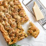 completed Vegan Cheesy Garlic Focaccia with a piece cut out against a white surface