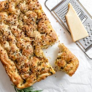 completed Vegan Cheesy Garlic Focaccia with a piece cut out against a white surface