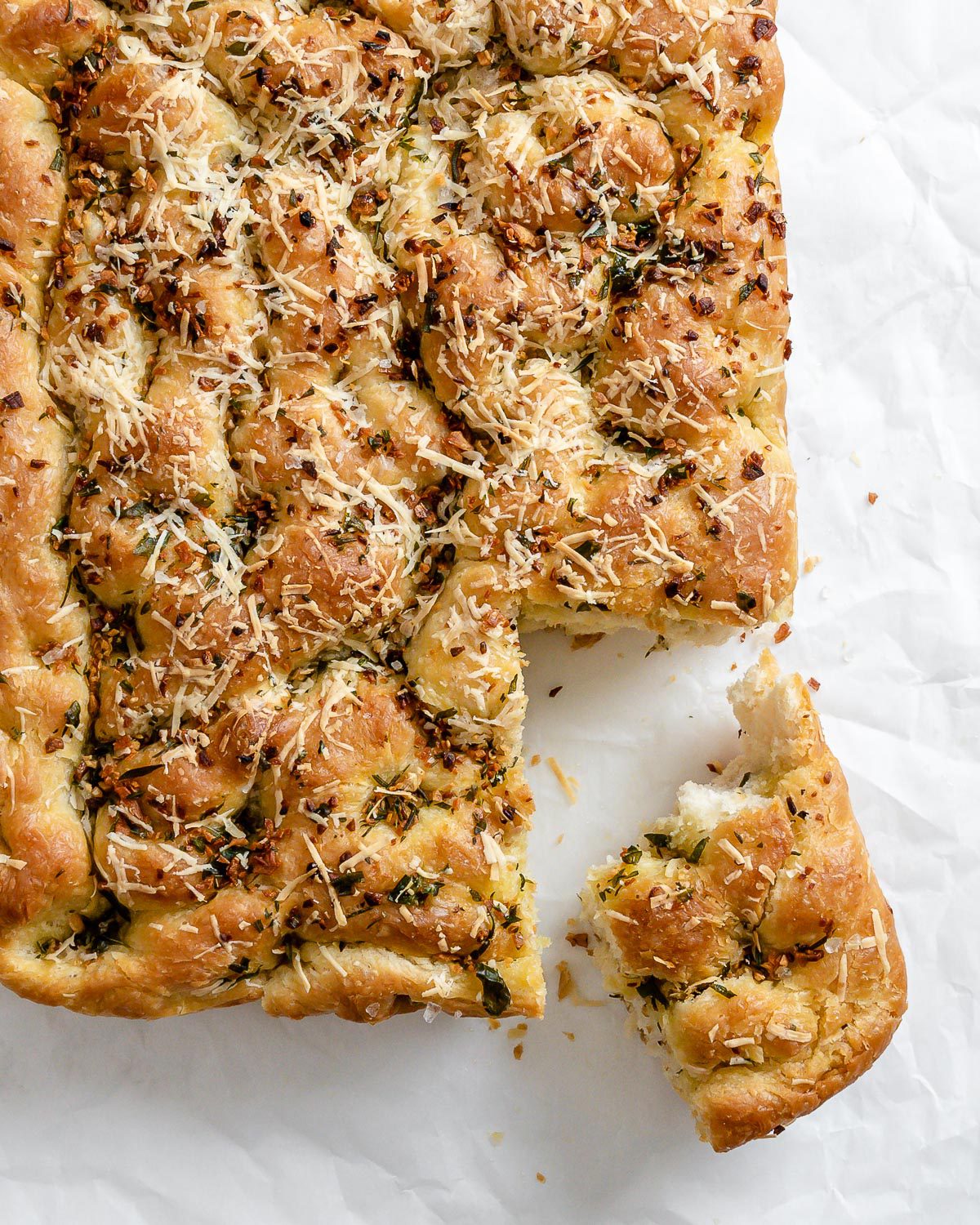 completed Vegan Cheesy Garlic Focaccia with a piece cut out against a white surface