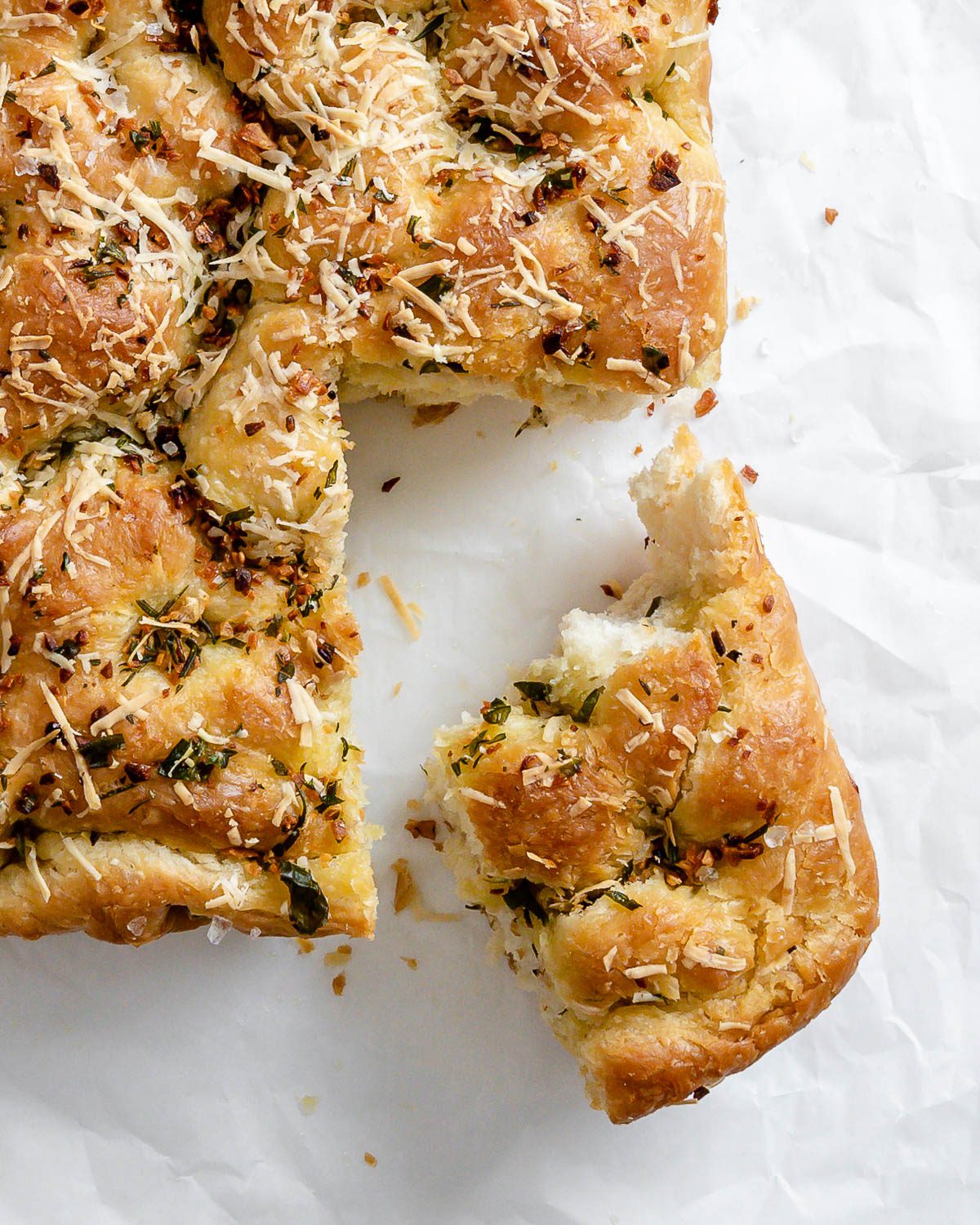 completed Vegan Cheesy Garlic Focaccia with a piece cut out against a white surface