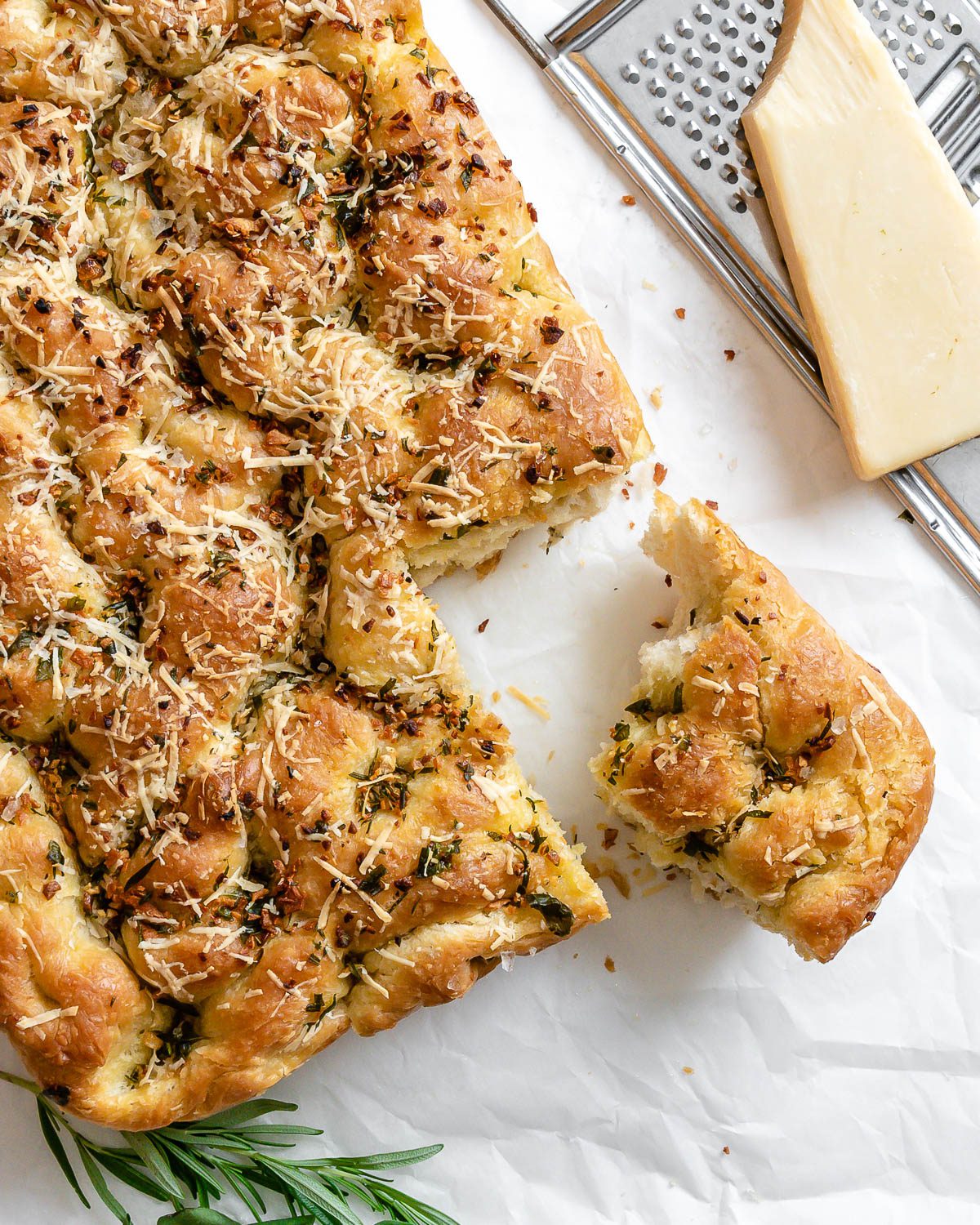 completed Vegan Cheesy Garlic Focaccia with a piece cut out against a white surface