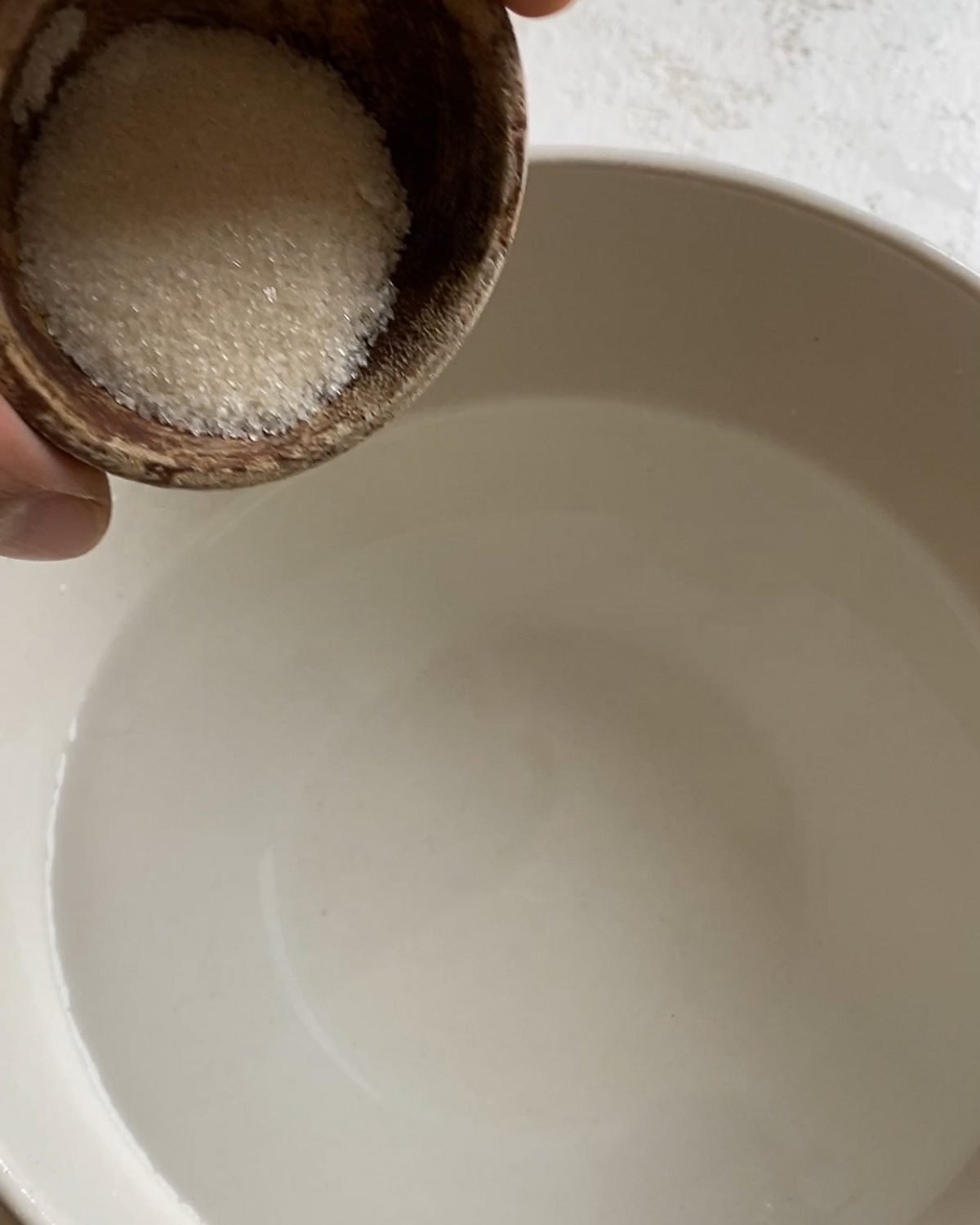 process of pouring sugar into a bowl of water